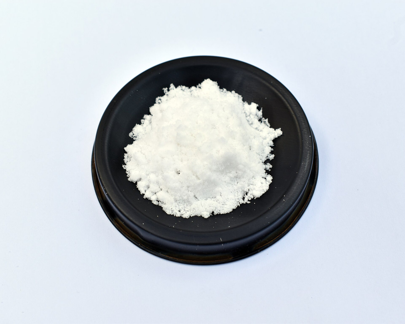 A heap of fine white crystalline powder in a black dish.