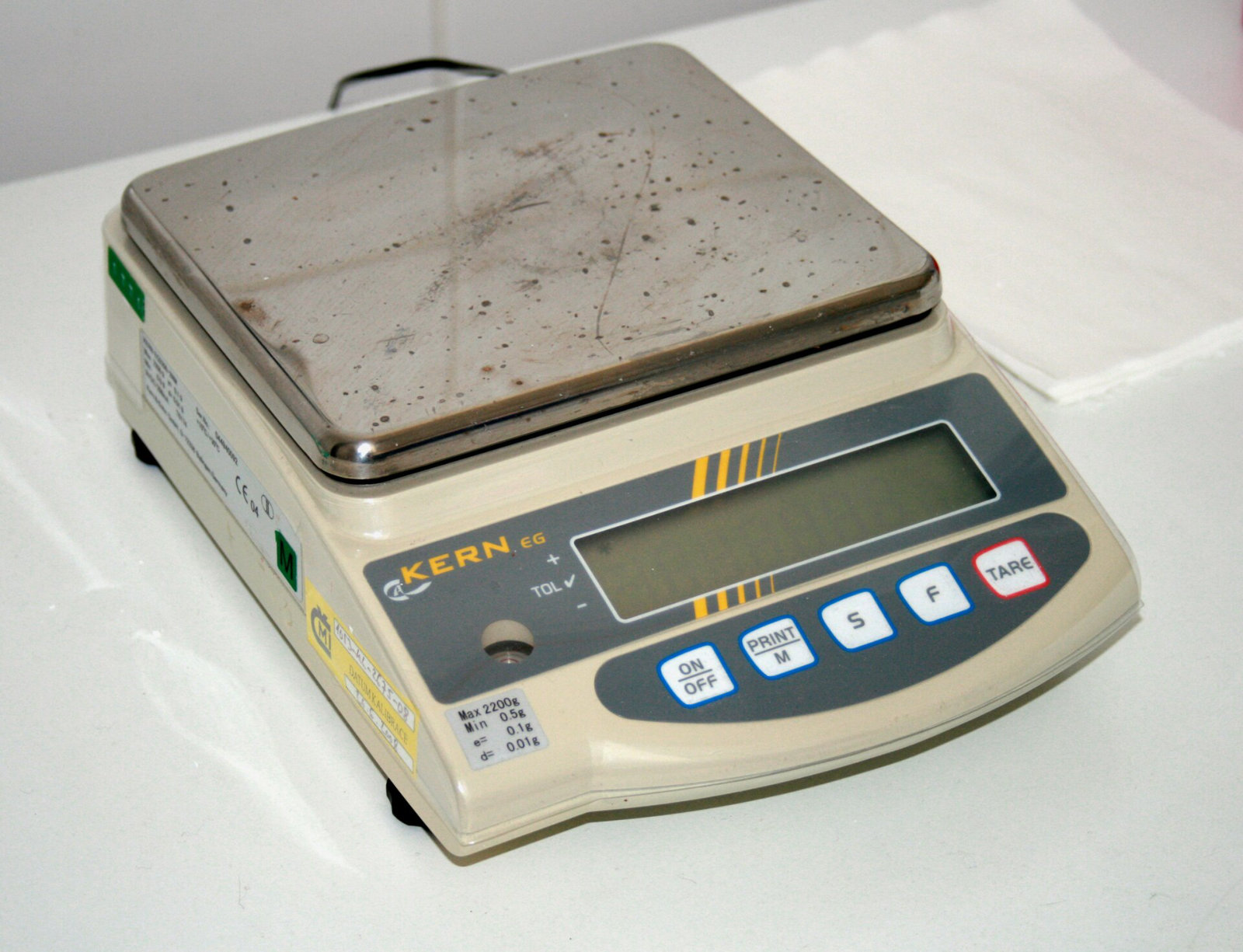 A cream-coloured electronic balance with a stainless steel pan and a keypad with a tare button.